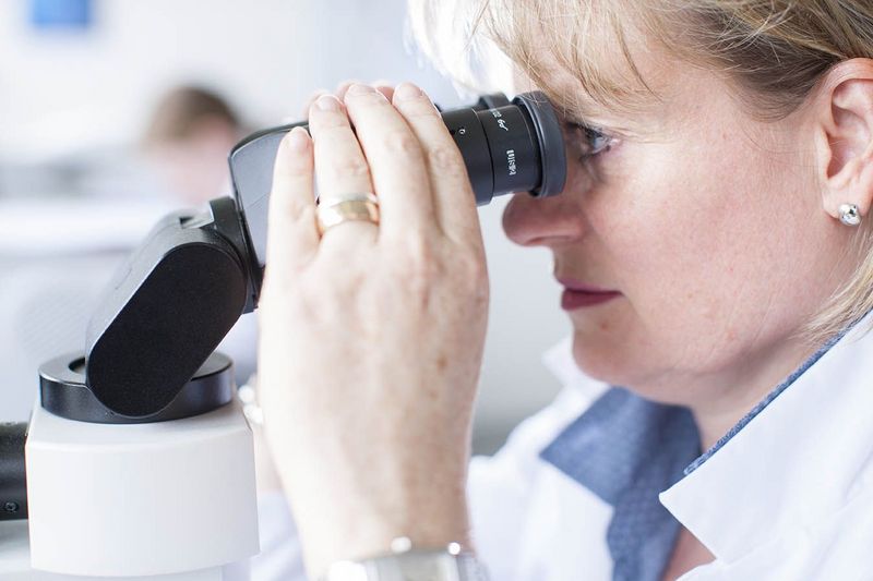 Labor-Mitarbeiterin blickt durch Mikroskop